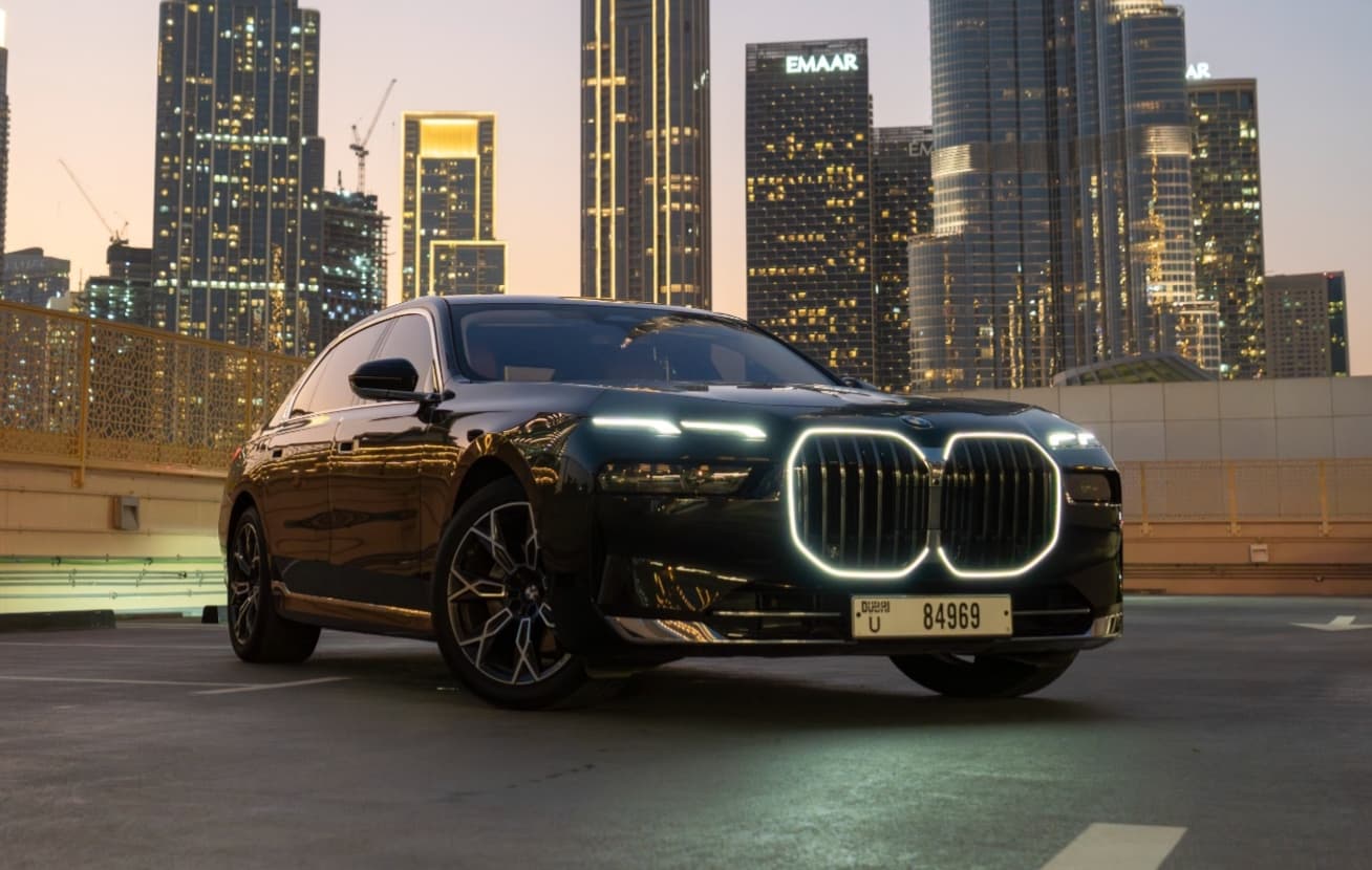 Vue extérieure avant trois-quarts de la BMW Série 7 avec calandre illuminée sur la skyline de Dubaï au crépuscule