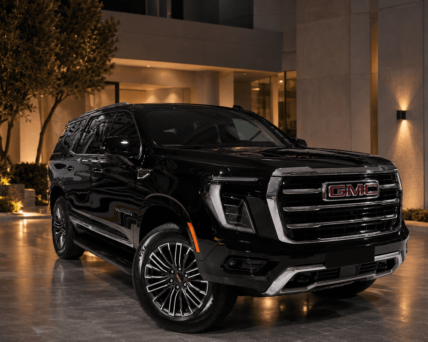 Vue extérieure avant trois-quarts du GMC Yukon Elevation devant une entrée moderne illuminée de nuit