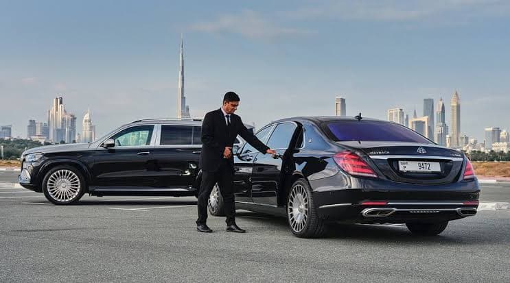 Chauffeur opening the door of a Mercedes-Maybach S-Class beside a GLS SUV with the Dubai skyline in the background