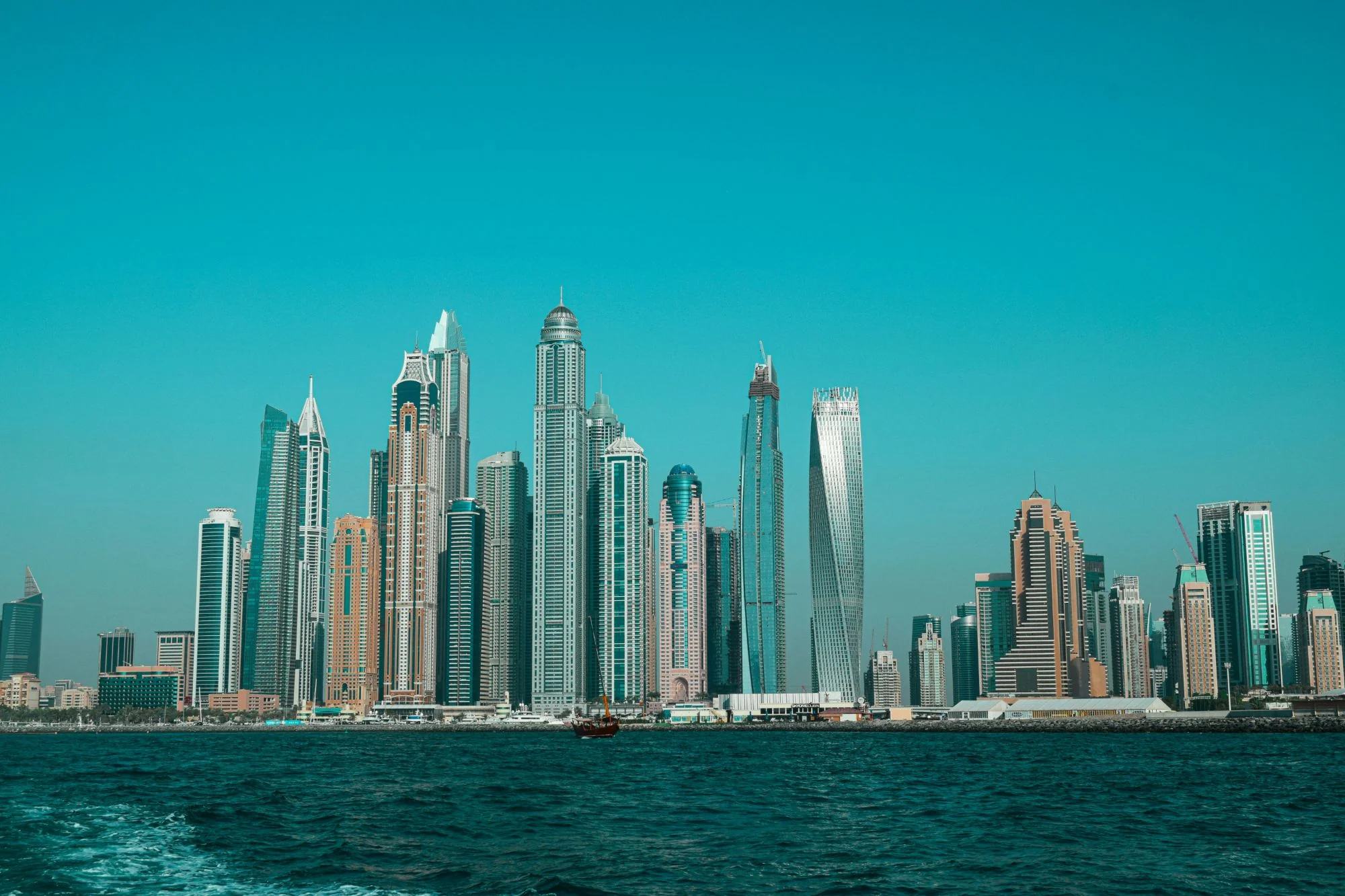 Dubai Marina skyline viewed from the water, with the Marina's towers under a clear teal sky